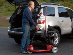 Man holding remote for Curb Sider lift in back of silver vehicle attached to red three wheel scooter