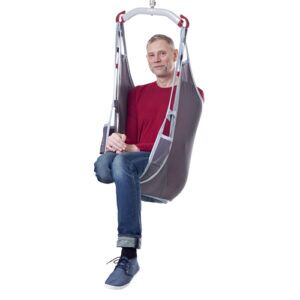A man in a red shirt and jeans is comfortably seated in a Molift EvoSling MediumBack Net Padded, isolated on a white background.